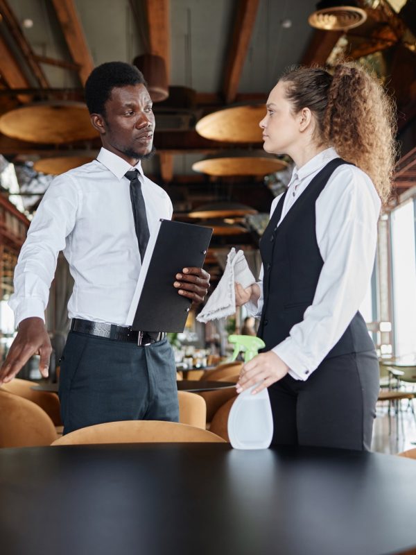 Black man as manager training servers cleaning dining room in restaurant